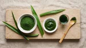 Overhead view of pandan powder, pandan paste, pandan liquid extract and fresh pandan leaves arranged on a wooden board