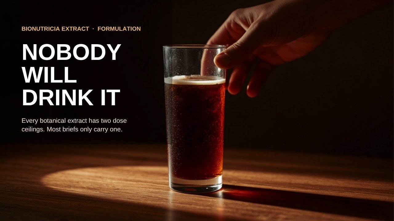 A hand withdrawing from a nearly untouched glass of dark botanical beverage on a warm-lit counter