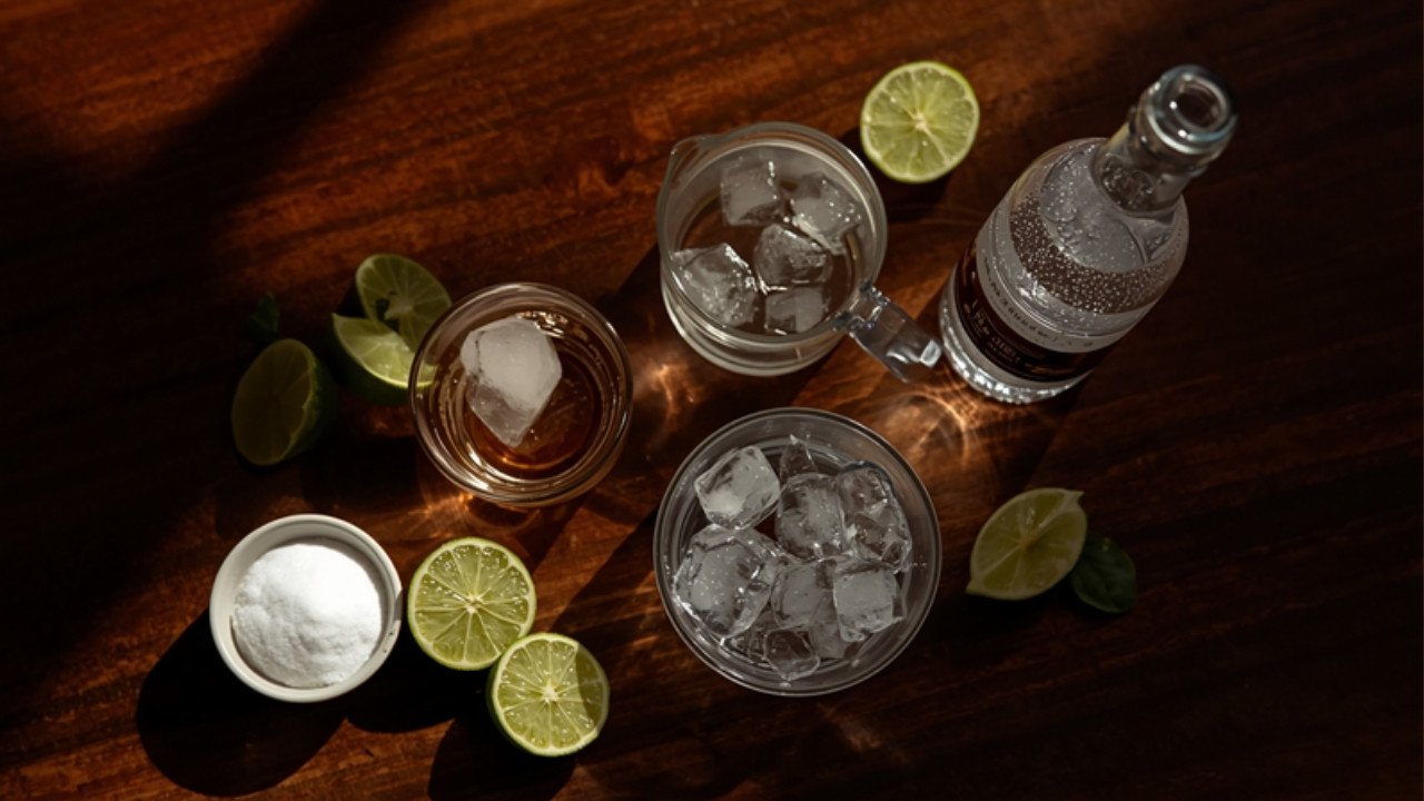 Sugar, limes, ice and sparkling water on a dark bench, overhead warm light